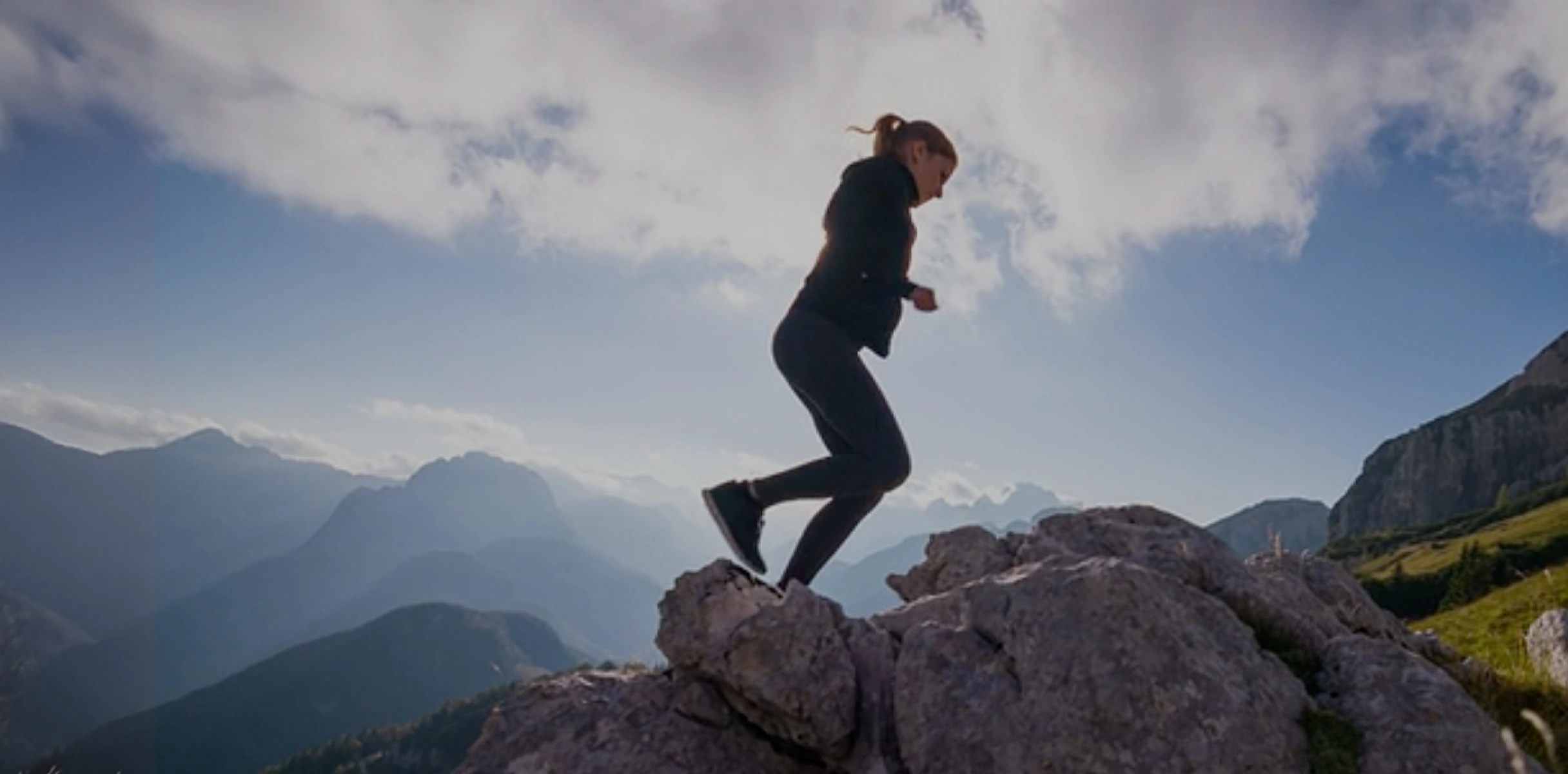 A woman dressed in athletic gear running up a mountain on a sunny day